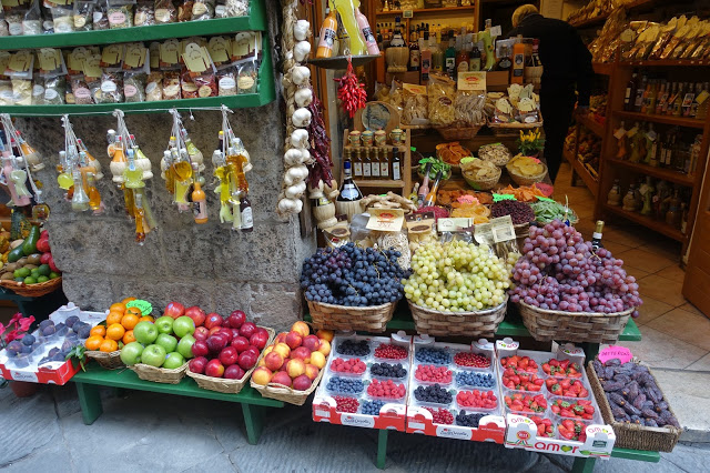 Bildet viser en liten butikk inne i Siena fylt med frukter og hvitløk. 